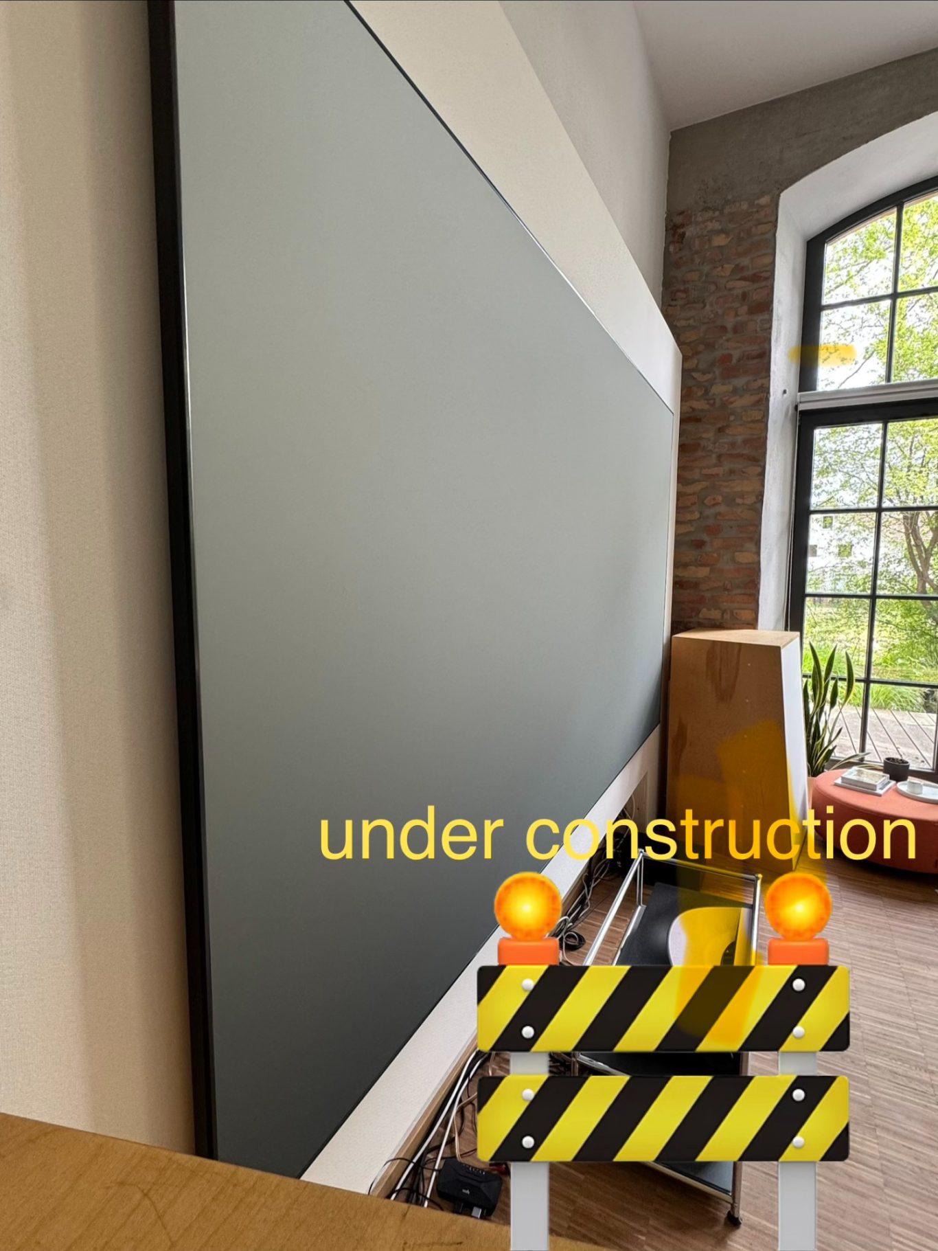Hisense L9Q an 120" CLR Wand mit grauer Leinwand, umgeben von Bauzubehör und einem Baustellenabsperrungsschild.