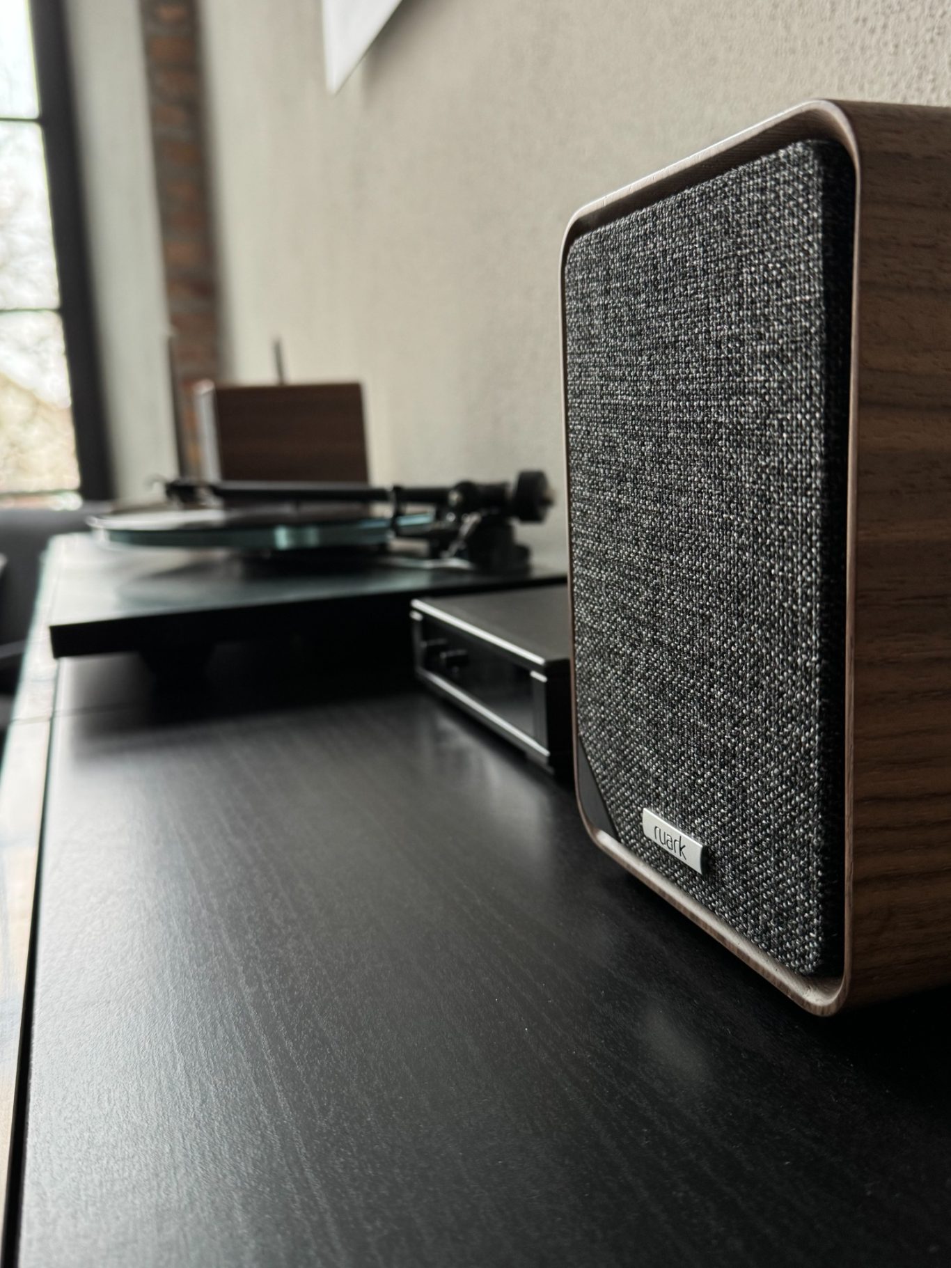 Rega P3RS Holzlautsprecher auf einem Tisch mit einem Plattenspieler im Hintergrund.