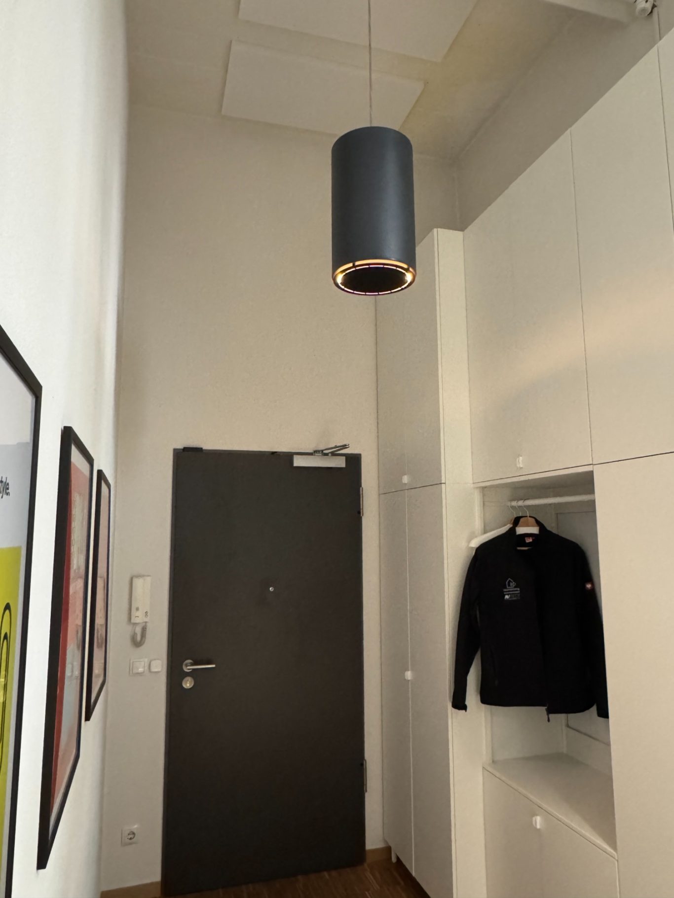 Garvan Pendellautsprecher Heller Flur mit einer grauen Deckenlampe mit integriertem Lautsprecher, schwarzem Kleidungsstück und einer Tür.